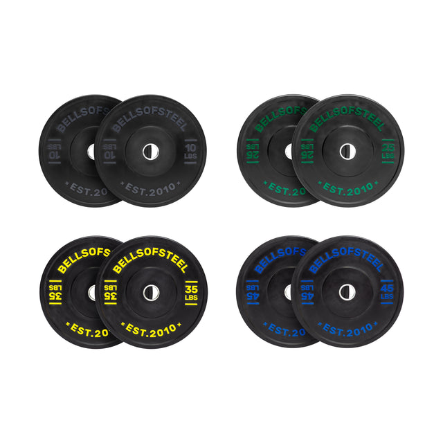 The Bells of Steel Dead Bounce Conflict Bumper Plate Sets include four pairs (10 lbs white, 25 lbs green, 35 lbs yellow, 45 lbs blue), each with colored markings, stainless steel insert rings, and “BELLS OF STEEL EST. 2010” labels, arranged in a grid.