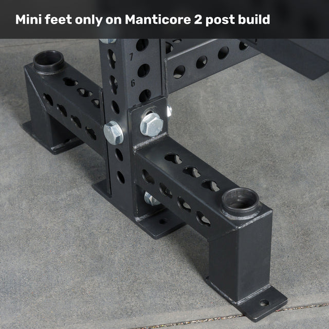Close-up of the base of a black metal Manticore Two Post Converter Bench by Bells of Steel USA, with mini feet secured by bolts on concrete. Top text: “Mini feet only on Manticore 2 post build.” Premium gym equipment for your space.