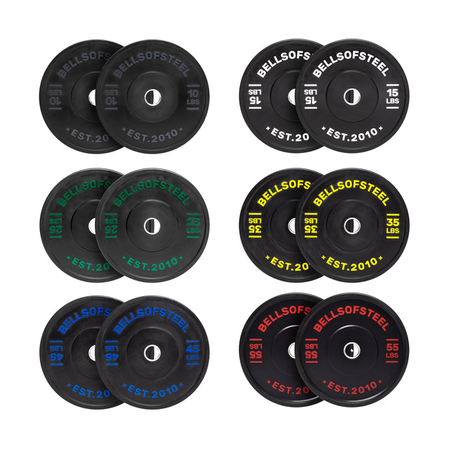 Eight pairs of black Bells of Steel Dead Bounce Conflict Bumper Plate Sets feature color-coded weight labels—10, 15, 25, 35, 45 & 55 lbs.—with stainless steel inserts for durability. Each pair is grouped with its corresponding color.