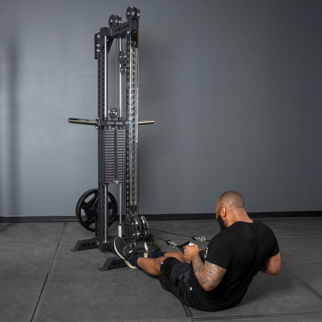 A man in black workout attire performs a seated row with a handle attachment on the Bells of Steel USA Oblivyon Tower - 3" x 3” Cable Tower in a minimalist gray gym space.