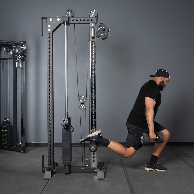 A man in athletic wear does a Bulgarian split squat with a dumbbell, resting one foot on the Bells of Steel USA Oblivyon Tower - 3" x 3” Cable Tower behind him and lowering his body with his other leg forward.