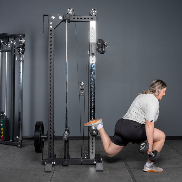 Wearing athletic gear, a person does a Bulgarian split squat with a dumbbell, placing one foot on the Bells of Steel USA Oblivyon Tower - 3" x 3” Cable Tower in the gym.