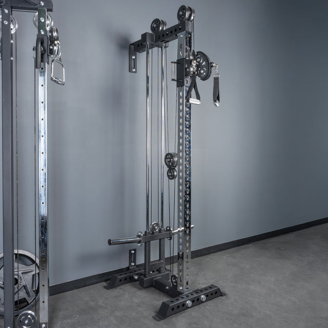 The Bells of Steel USA Oblivyon Tower - 3" x 3” Cable Tower, with adjustable pulleys and handles, stands against a gray wall. Its sturdy metal build and various weight options make it perfect for versatile gym workouts.