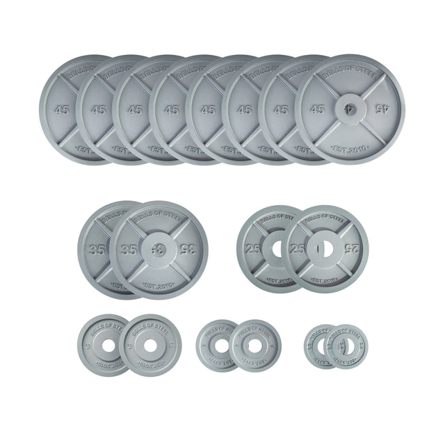 Bells of Steel Machined Iron Olympic Weight Plate Sets in gray, with engraved weight values and brand markings, feature precision holes and a slim design. Plates of various sizes and weights are arranged in rows on a white background.