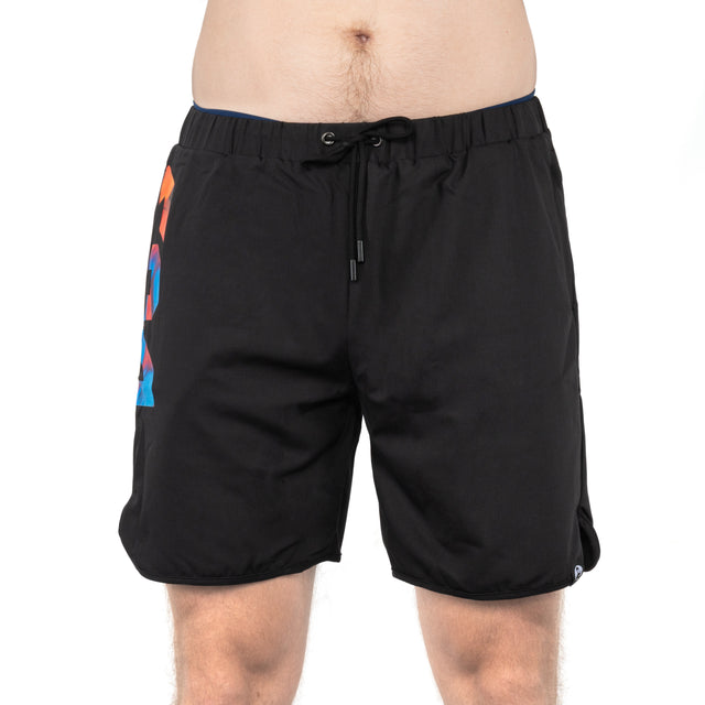 A person wearing Bells of Steel Gym Shorts with black stretchy fabric and a colorful geometric design on the left side stands against a white background, showing only their lower torso and upper legs.