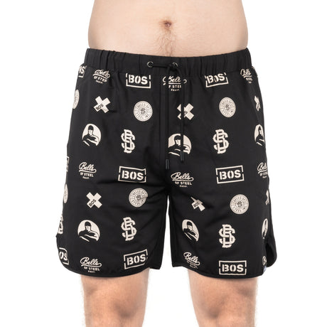 A person in Bells of Steel Gym Shorts, featuring a drawstring, white "BOS" and "Bells of Steel" logos, and graphic designs on stretchy black fabric, stands against a plain white background.