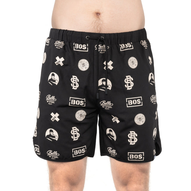 A person in Bells of Steel Gym Shorts, featuring a drawstring, white "BOS" and "Bells of Steel" logos, and graphic designs on stretchy black fabric, stands against a plain white background.