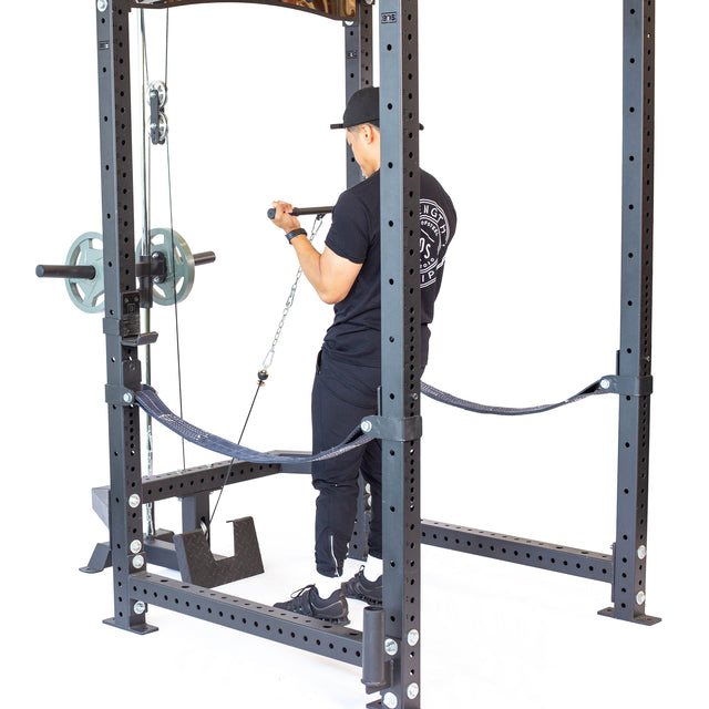 A person in black workout gear uses the Bells of Steel Lat Pulldown & Low Row Rack Attachment – Hydra & Manticore on a gym rack to perform a seated row with a straight bar, demonstrating effective cable exercises. The background is white.
