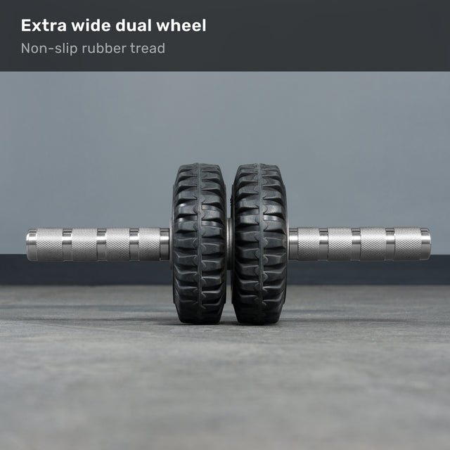 The ABsyidyan Stainless Steel Ab Roller by Bells of Steel USA, featuring extra-wide dual wheels and a 500 lb capacity, stands upright on a gray floor. Text above reads: "Extra wide dual wheel. Non-slip rubber tread.
