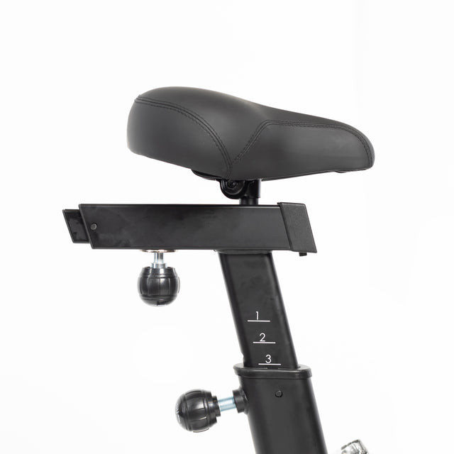 Close-up of a black adjustable seat on the Bells of Steel Residential Air Bike with Wind Guard, perfect for your home gym. The seat is supported by a numbered metal post for height adjustment, secured by two knobs. Its sleek design stands out against a plain white background.