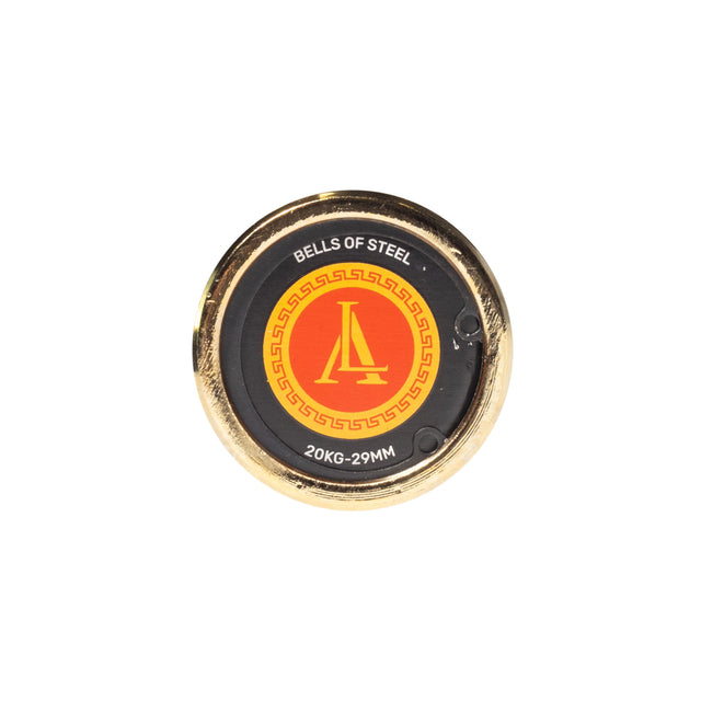 The Alex Leonidas Onyx Bar by Bells of Steel is a round, gold-colored plate with a black center, Cerakote finish, red and yellow logo, and “BELLS OF STEEL” plus “20KG-29MM” printed on it.