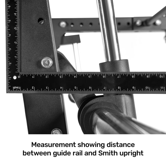 A close-up shows a metal ruler measuring the distance between a guide rail and the Bells of Steel Smith Machine Rack Attachment. The black ruler, featuring white markings and numbers, highlights the precise measurement vital for aligning your power rack setup.