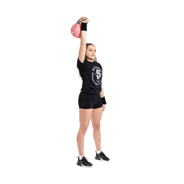 A person in black athletic wear demonstrates a fitness exercise on one leg, lifting a pink kettlebell overhead while wearing Bells of Steel BellGuard Kettlebell Wrist Guards (Pair) against a plain white background.