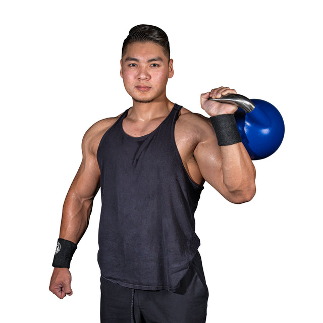 A muscular man wearing Bells of Steel BellGuard Kettlebell Wrist Guards pairs his black tank top with a blue kettlebell on his shoulder, posing confidently against a white background.