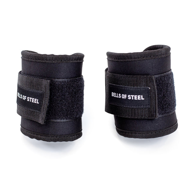 Two black wrist wraps with Velcro closures display "BELLS OF STEEL" on a plain white background. Perfect for wrist support during weightlifting, they complement the Bells of Steel Adjustable Ankle Strap Cable Attachment for full-body workouts on the cable machine.