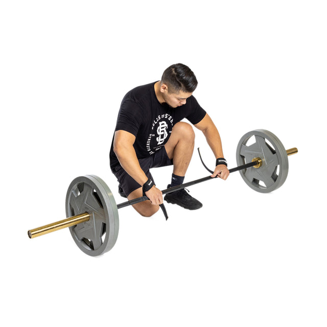 A man kneels on one knee, preparing to deadlift a barbell loaded with heavy plates as he wraps Bells of Steel Lifting Straps around the bar to enhance his grip strength.
