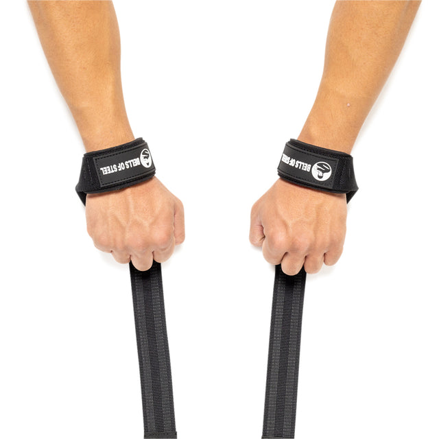 Two hands wearing Bells of Steel wrist straps hold black Lifting Straps, designed to improve grip strength, against a white background.