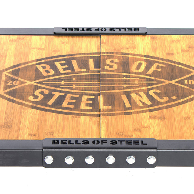 The Bells of Steel Deadlift Platform Bamboo Insert features a durable wooden build with a centered engraved logo, black metal edges, sturdy bolts, and a bamboo insert for enhanced stability.