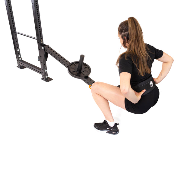 A woman in black workout gear expertly squats using the Bells of Steel Belt Squat/Lever Arms Rack Attachment connected to a landmine barbell plate on a sturdy gym rack. Set against a white background, it’s perfect inspiration for any home gym.