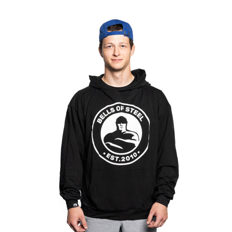 A young man in a blue backward cap and a black Bells of Steel Bamboo Hoodie stands against a plain white background, smiling gently at the camera.