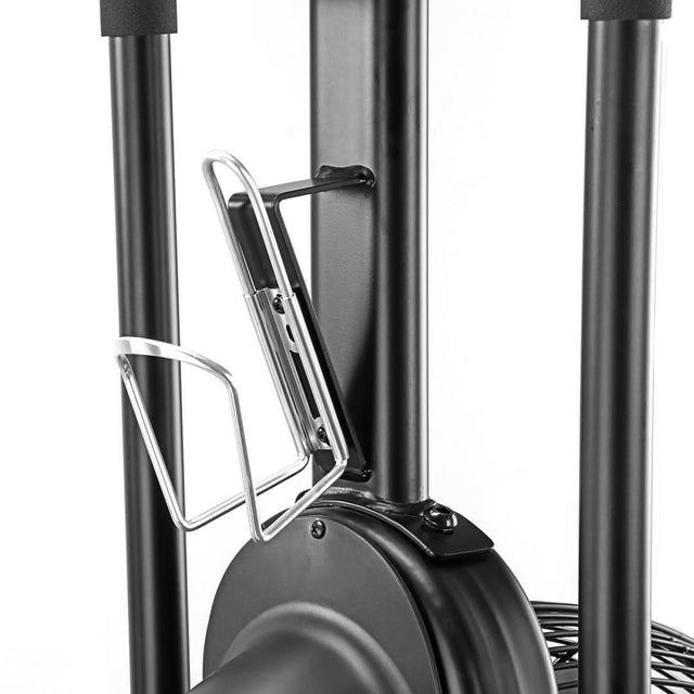 Close-up of a metal water bottle holder mounted on the frame of the Bells of Steel Blitz Air Bike, a black air bike featured in a home gym setup with a white background.