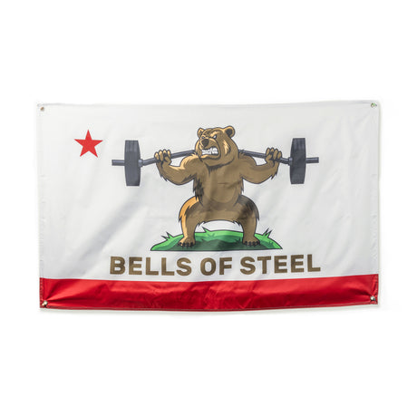 The Bells of Steel Flags feature a cartoon bear on grass lifting a barbell, with a red star and bottom stripe. "BELLS OF STEEL" is boldly written—ideal for adding unique flair to your home gym decor.