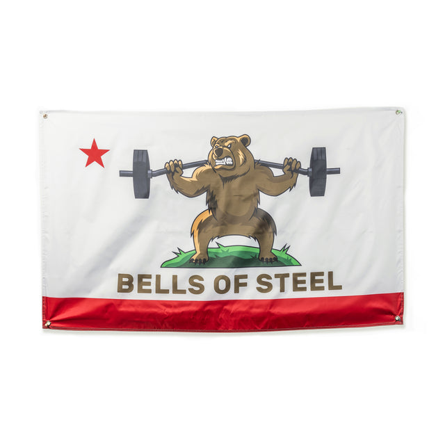 The Bells of Steel Flags feature a cartoon bear on grass lifting a barbell, with a red star and bottom stripe. "BELLS OF STEEL" is boldly written—ideal for adding unique flair to your home gym decor.