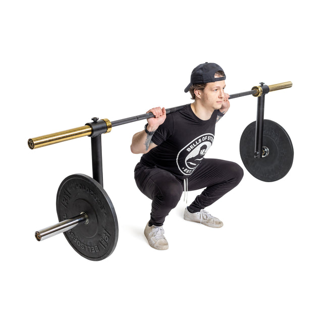 A person wearing black clothing and white shoes performs a squat with the Bells of Steel Camber Bar Attachment - Pair, engaging their stabilizer muscles, isolated on a white background.