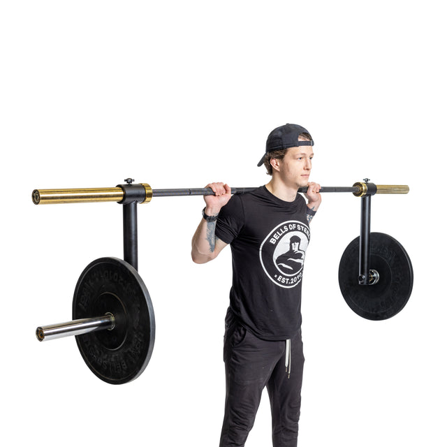 A person uses the Bells of Steel Camber Bar Attachment - Pair, holding an Olympic barbell with large weights on their shoulders, preparing for a squat and engaging stabilizer muscles, against a white background.