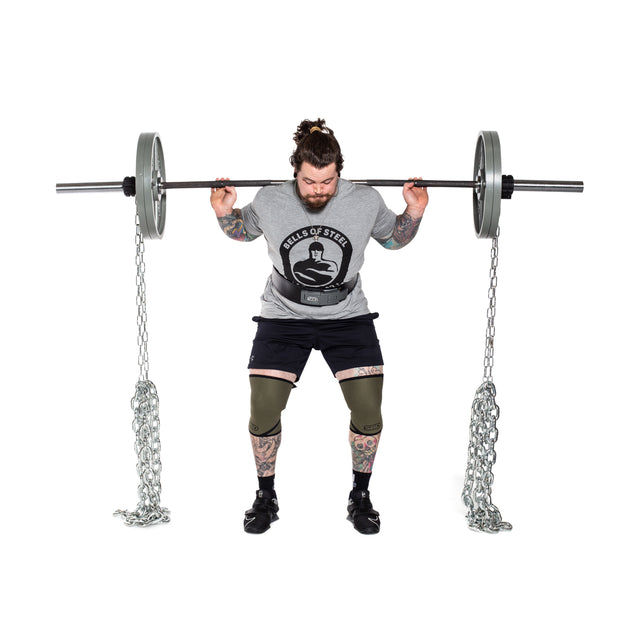 A man with tattoos and knee sleeves squats with a barbell and Bells of Steel Weightlifting Chains, demonstrating progressive resistance against a white background.
