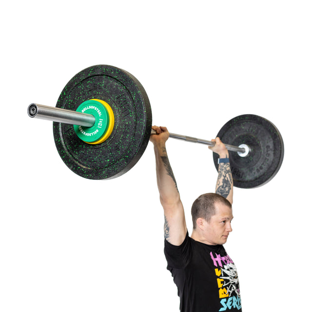 A tattooed man in a black graphic t-shirt lifts a heavy barbell with Bells of Steel Urethane-Coated Change Plates overhead, standing against a white background.