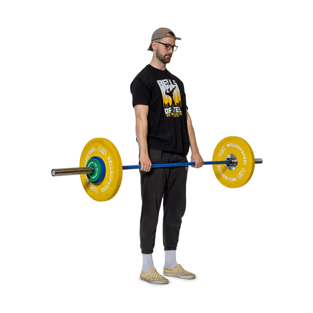A man in a cap, glasses, black T-shirt and pants, and checkered slip-ons holds a barbell with Bells of Steel Urethane-Coated Change Plate Sets, standing against a white background.