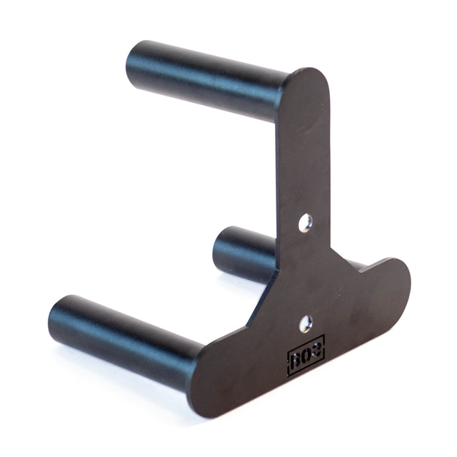 The Bells of Steel Change Plate Storage Pegs feature a black metal bracket with two horizontal rods and one vertical rod for Olympic change plates, mounted on a flat base with screw holes and the brand's rectangular logo on the front.