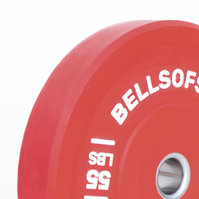 A close-up of a red Bells of Steel Colored Bumper Plate Set labeled "BELLSOFSTEEL" and "55 LBS" in white, showing the stainless steel insert and plate edge on a white background.
