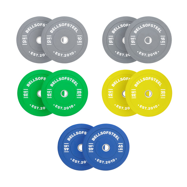 The Bells of Steel Colored Bumper Plate Sets feature accurate weights with stainless steel inserts. Plates—grey (10, 25 LB), green (25 LB), yellow (35 LB), blue (45 LB)—each display “Bells of Steel” and “EST. 2010.”.