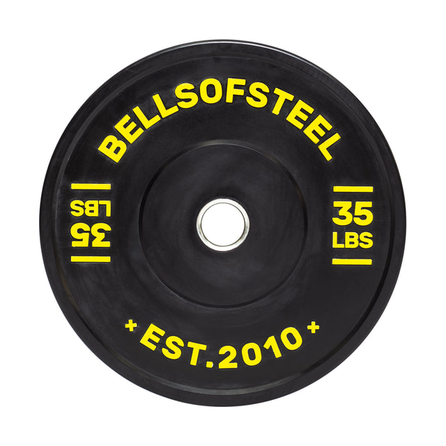 The Dead Bounce Conflict Bumper Plate from Bells of Steel is a black virgin rubber plate featuring yellow text with "BELLSOFSTEEL" at the top, "35 LBS" on both sides, and "EST. 2010" at the bottom. It includes a stainless steel insert for durability.
