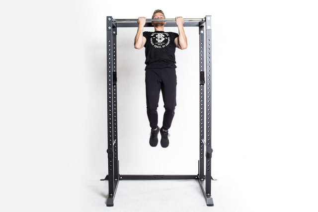 A person in black T-shirt and pants does a pull-up on the Bells of Steel Residential Power Rack (2.3" x 2.3", ⅝" holes) with J-cups, set against a plain white background—ideal inspiration for your home gym setup.