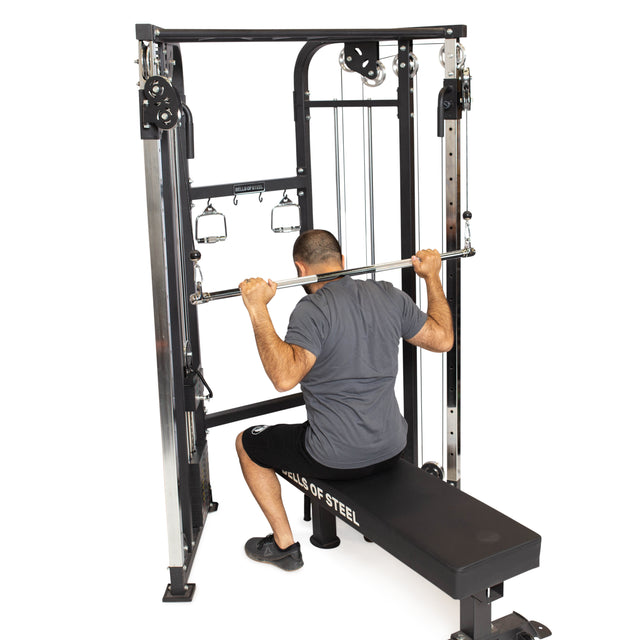 Wearing a gray shirt and black shorts, a person sits on a bench performing a lat pulldown by pulling the Bells of Steel Double Hook Straight Bar Cable Attachment behind their neck.