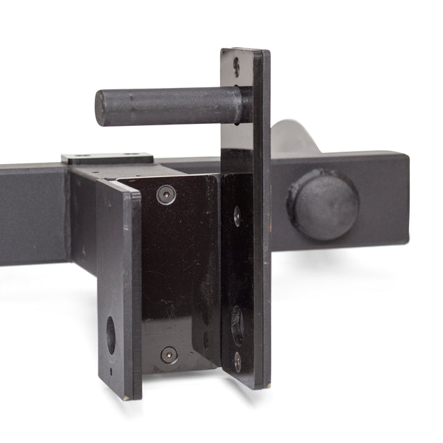 Close-up of the Y Dip Bar Rack Attachment by Bells of Steel, featuring a heavy-duty black metal hitch receiver with a locking pin. The design includes two metal plates with circular holes and one plate showing a protruding pin against a plain white surface.