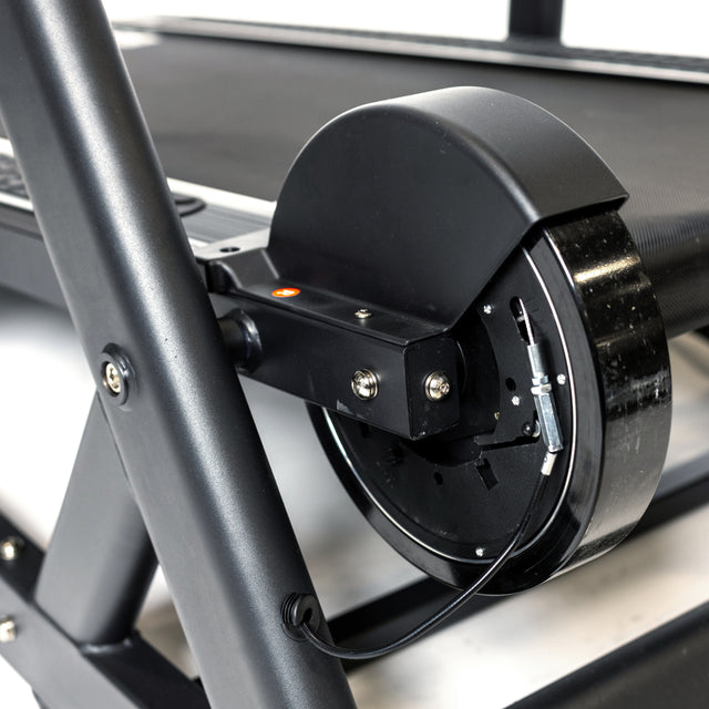Close-up of The Dreadmill's incline mechanism by Bells of Steel, showcasing a black motor and gear assembly linked to the treadmill belt. The metallic frame features visible screws and cables, highlighting the intricate engineering typical of high-performance treadmills.