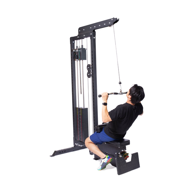 A person uses the Bells of Steel Multi Grip Curl Bar Cable Attachment on a gym lat pulldown machine, grasping it with both hands to effectively isolate arm muscles. They wear a black shirt, blue shorts, and colorful sneakers.