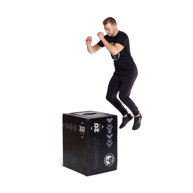 A man in athletic wear jumps from the Bells of Steel 6-In-1 Soft Foam Plyo Box / Squat Box, labeled with 20" and 30" heights, demonstrating versatile exercises against a white background.