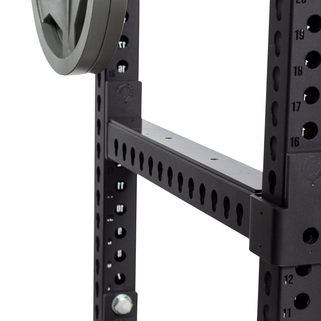 Close-up of Bells of Steel Flip-Down Safeties attached to a black metal power rack with numbered adjustment holes for precise height and safe training; a weight plate is visible on the left.