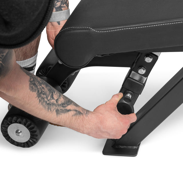 A person adjusts the angle of the Bells of Steel Flat/Incline/Decline Weight Bench - Commercial by pulling a lever, their athletic gear showing readiness to use this versatile bench for targeted muscle training.