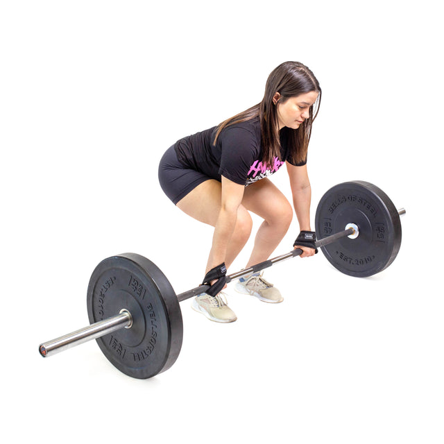 Wearing Bells of Steel Classic Figure 8 Lifting Straps, a woman squats to grip a barbell in deadlift position, testing her grip strength.