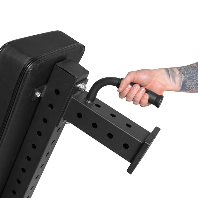 A tattooed hand grips the adjustment handle of the Bells of Steel Powerlifting Flat Bench, showing its angle adjustment mechanism and highlighting its sturdy 1,000lb max capacity.