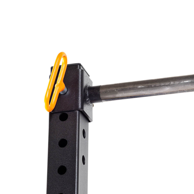 Close-up of a Bells of Steel Folding Rack 2.3" x 2.3" (5/8" Holes) wall-mounted in a garage gym, holding a barbell. An orange safety pin secures the adjustable black bracket to the post, which has multiple holes for easy height adjustment.