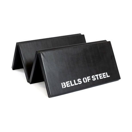 Two black Bells of Steel Four Fold Mats, one with a white "BELLS OF STEEL" logo, are shown partially unfolded and stacked together.