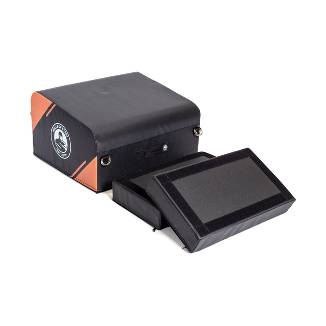 The Bells of Steel Soft Glute Bench is a black and orange rectangular padded bench with a side logo and two detachable foam pads secured by Velcro—ideal for home glute workouts, shown against a white background.