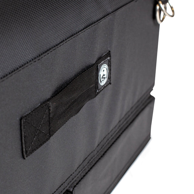 Close-up of a black Bells of Steel Soft Glute Bench bag with a small handle, stitched circular logo label, and metal rings. Perfect for carrying your glute bench accessories for an effective home workout.